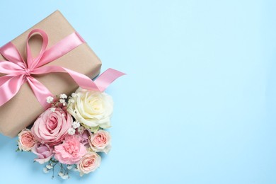 Gift box and beautiful flowers on light blue background, flat lay. Space for text