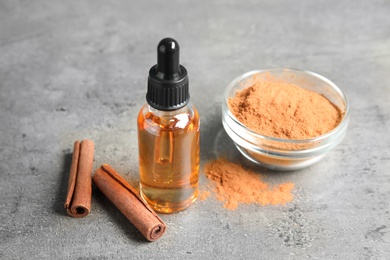 Photo of Bottle of essential oil, cinnamon sticks and powder on grey table