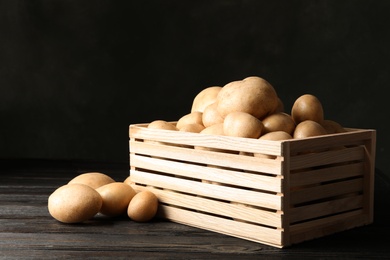 Photo of Raw fresh organic potatoes on wooden table against dark background. Space for text