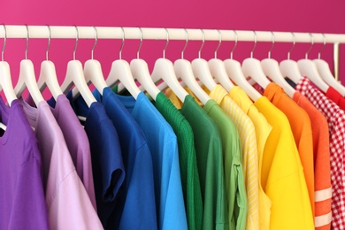 Rack with rainbow clothes on color background