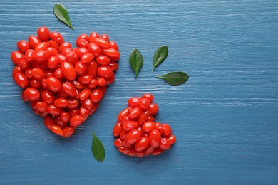 Heart shaped piles of fresh ripe goji berries on blue wooden table, flat lay