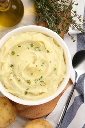Bowl of tasty mashed potato with rosemary and olive oil on beige wooden table, flat lay
