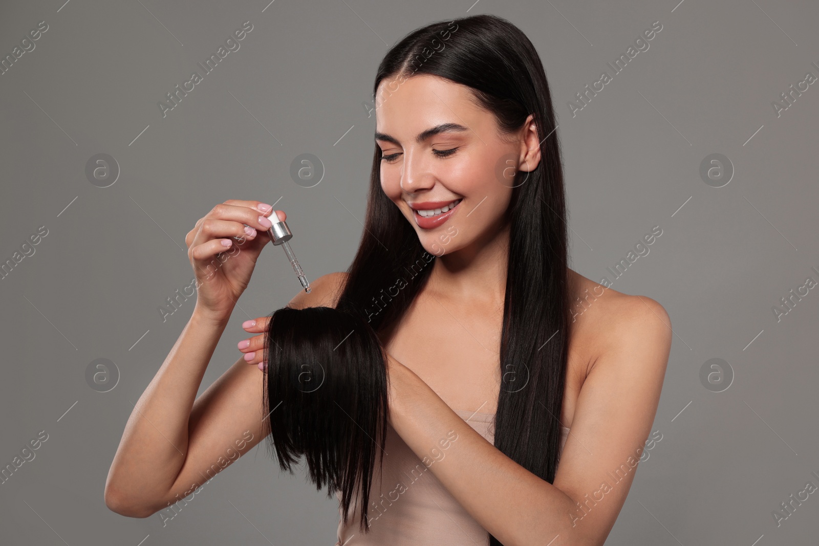 Photo of Beautiful woman applying hair serum on grey background. Cosmetic product