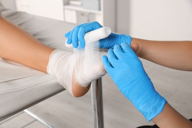 Doctor applying bandage onto patient's foot in hospital, closeup