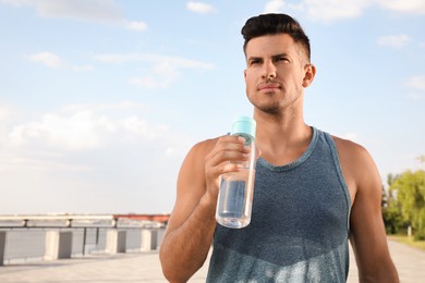 Handsome man in sportswear with bottle of water  outdoors on sunny day