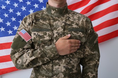 Soldier holding hand on heart near United states of America flag on white background, closeup