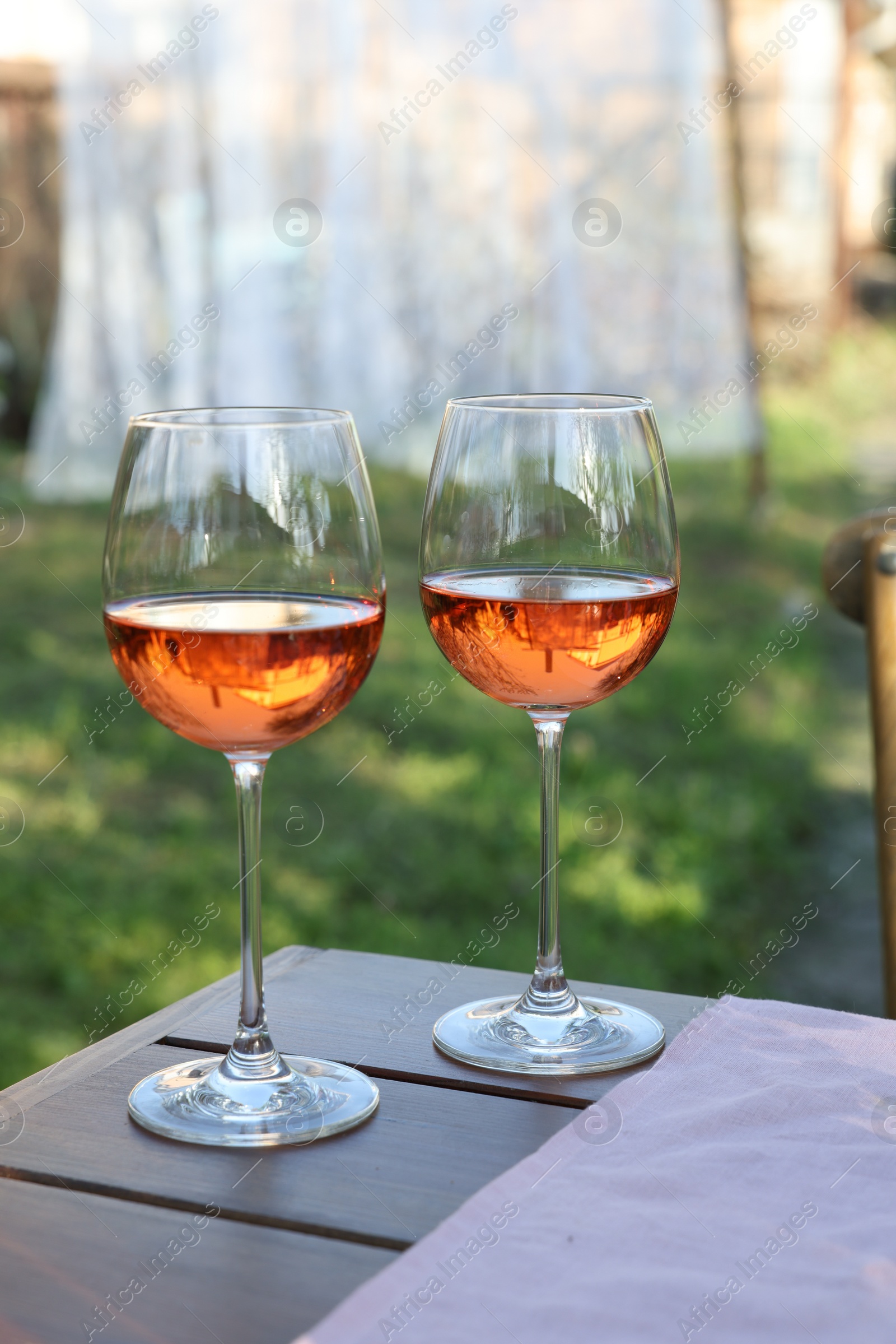 Photo of Glasses of rose wine on wooden table in garden