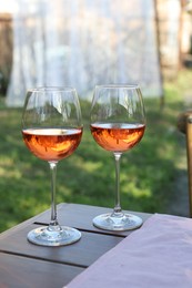 Glasses of rose wine on wooden table in garden