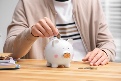 Man putting coin into piggy bank at wooden table, closeup