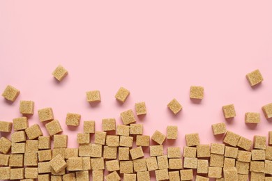 Brown sugar cubes on pink background, flat lay. Space for text