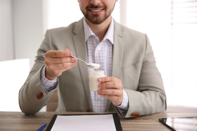 Photo of Happy young man with tasty yogurt at table indoors, closeup
