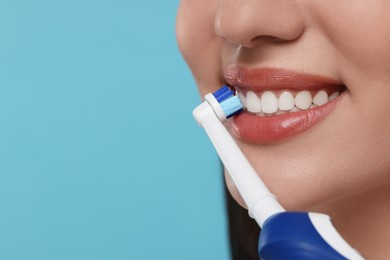 Photo of Woman brushing her teeth with electric toothbrush on light blue background, closeup. Space for text