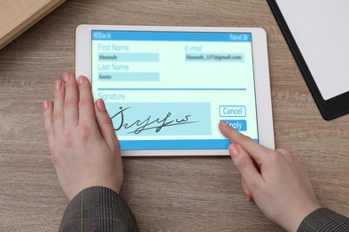 Image of Electronic signature. Woman using tablet at wooden table, closeup