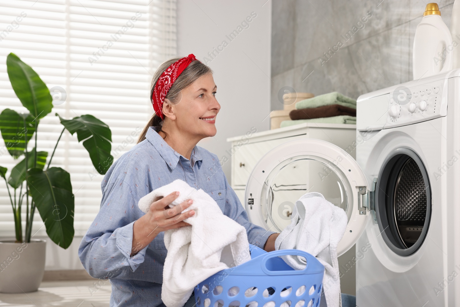 Photo of Happy housewife with laundry basket near washing machine at home