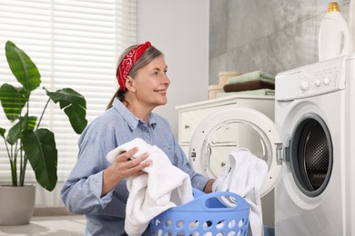 Happy housewife with laundry basket near washing machine at home