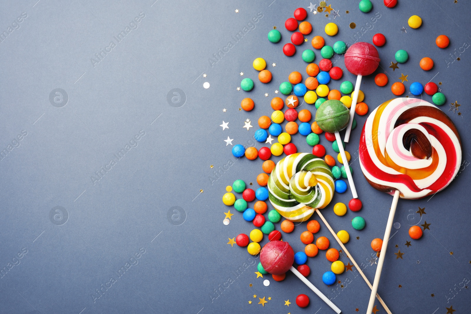 Photo of Lollipops and colorful candies on grey background, top view. Space for text