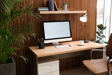 Comfortable workplace with computer near wooden wall in stylish room interior. Home office design