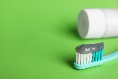 Brush with charcoal toothpaste on green background, closeup. Space for text