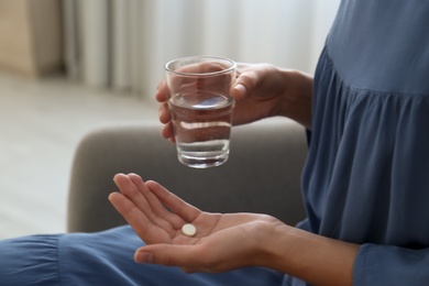 Photo of Woman holding glass of water and pill at home, closeup