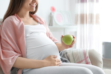 Photo of Young pregnant woman holding apple at home