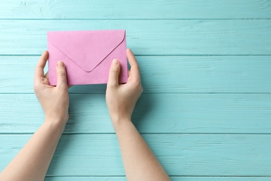 Woman with pink paper envelope at light blue wooden table, top view. Space for text