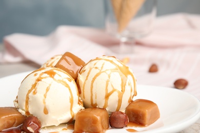 Photo of Delicious ice cream served with caramel, sauce and hazelnuts on table, closeup. Space for text