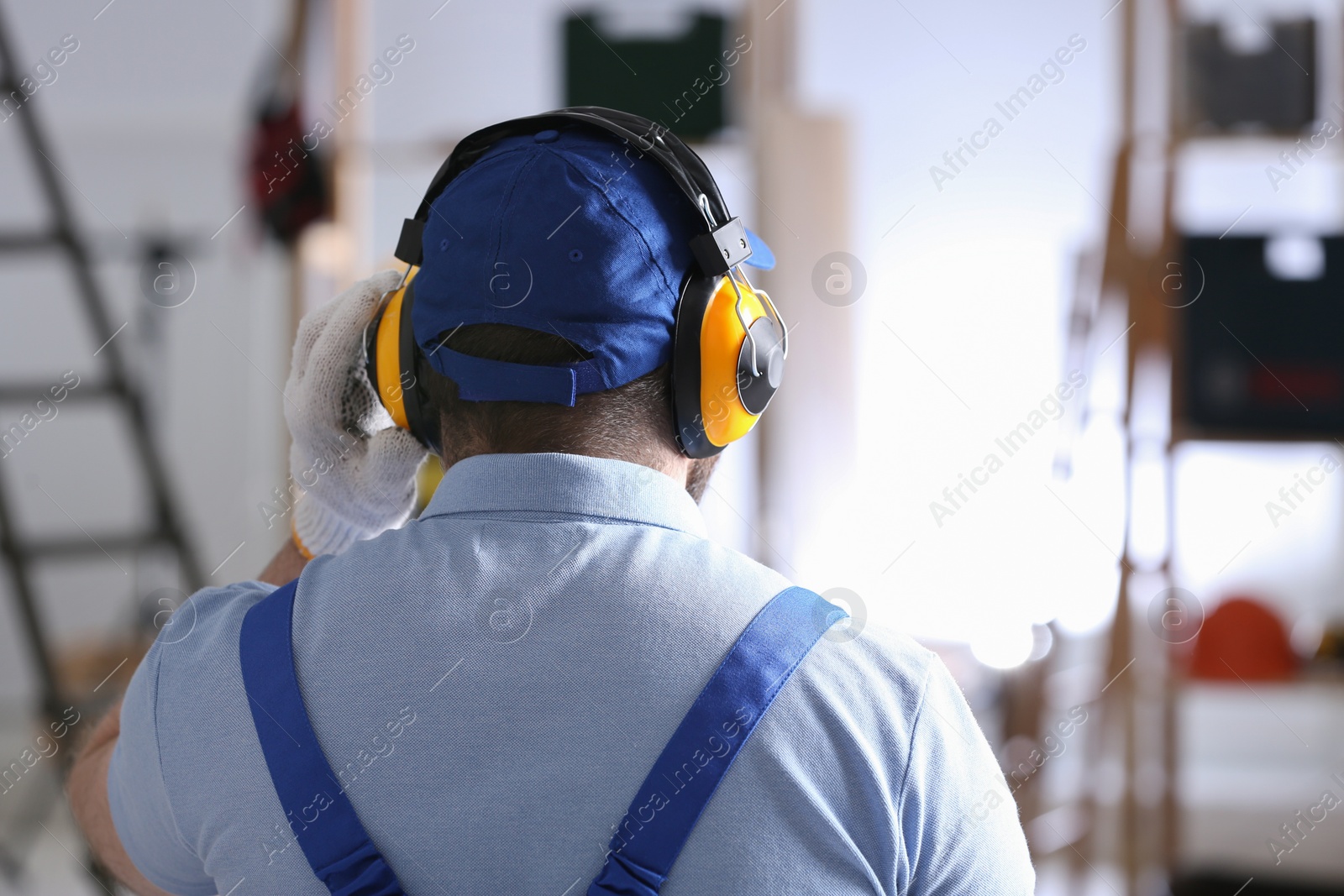 Photo of Worker wearing safety headphones indoors, back view. Hearing protection device