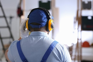 Worker wearing safety headphones indoors, back view. Hearing protection device