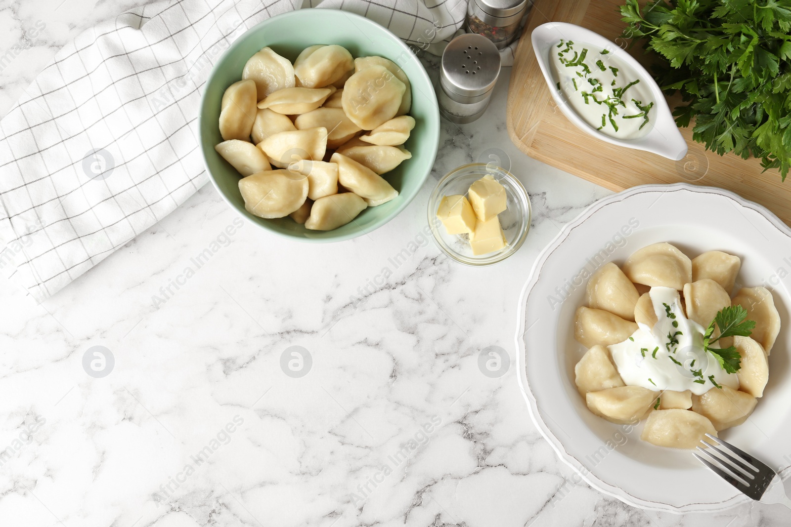 Photo of Delicious cooked dumplings with sour cream on white marble table, flat lay. Space for text