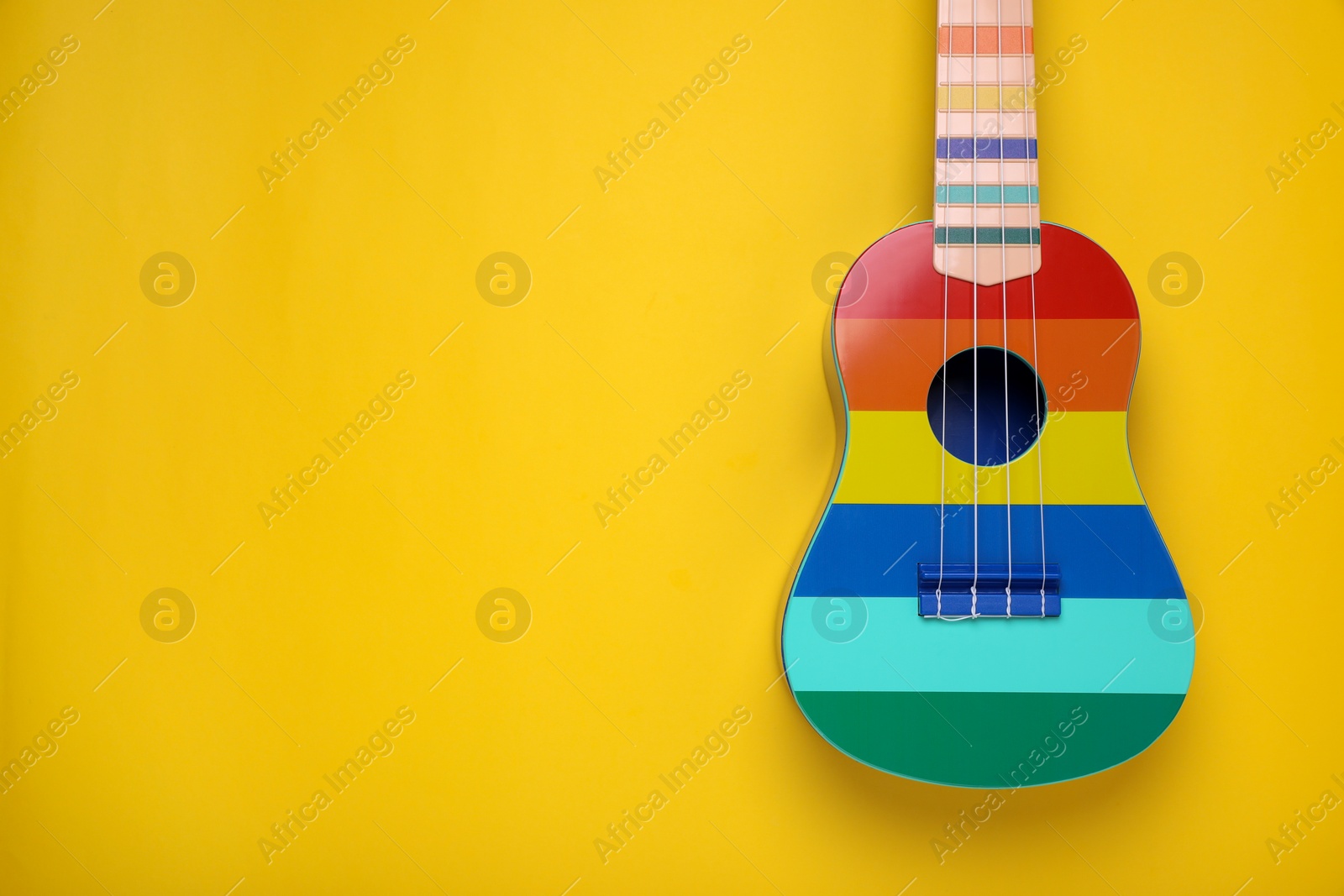 Photo of Colorful ukulele on yellow background, top view with space for text. String musical instrument