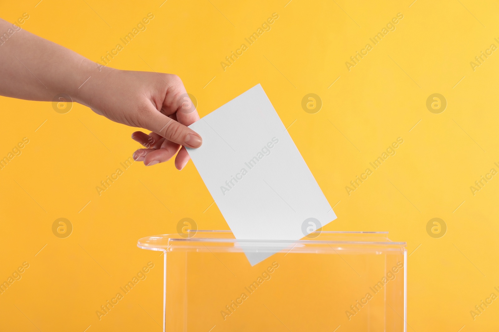 Photo of Woman putting her vote into ballot box on orange background, closeup