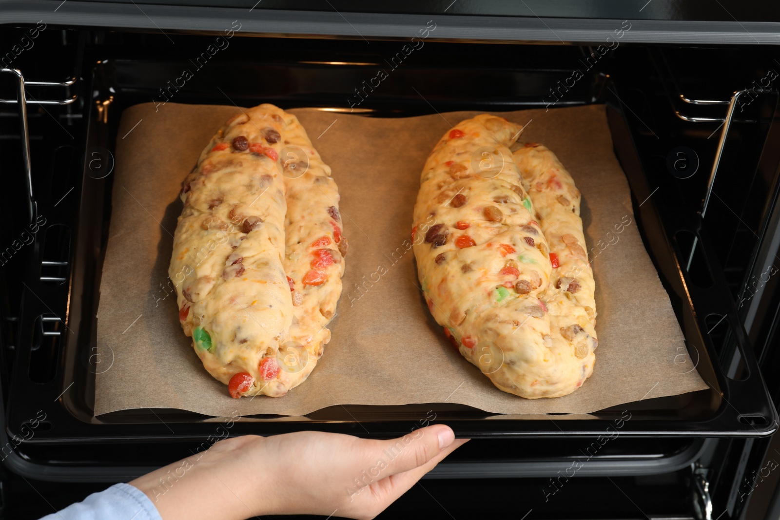 Photo of Woman putting baking tray with raw homemade Stollens into oven, closeup. Traditional German Christmas bread