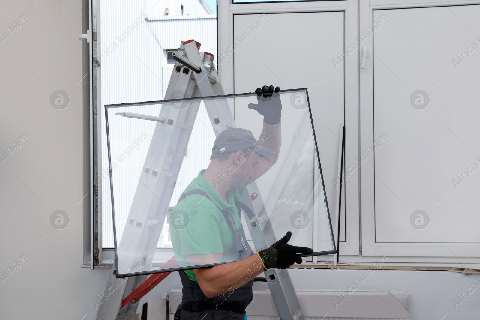 Photo of Worker near folding ladder installing window indoors