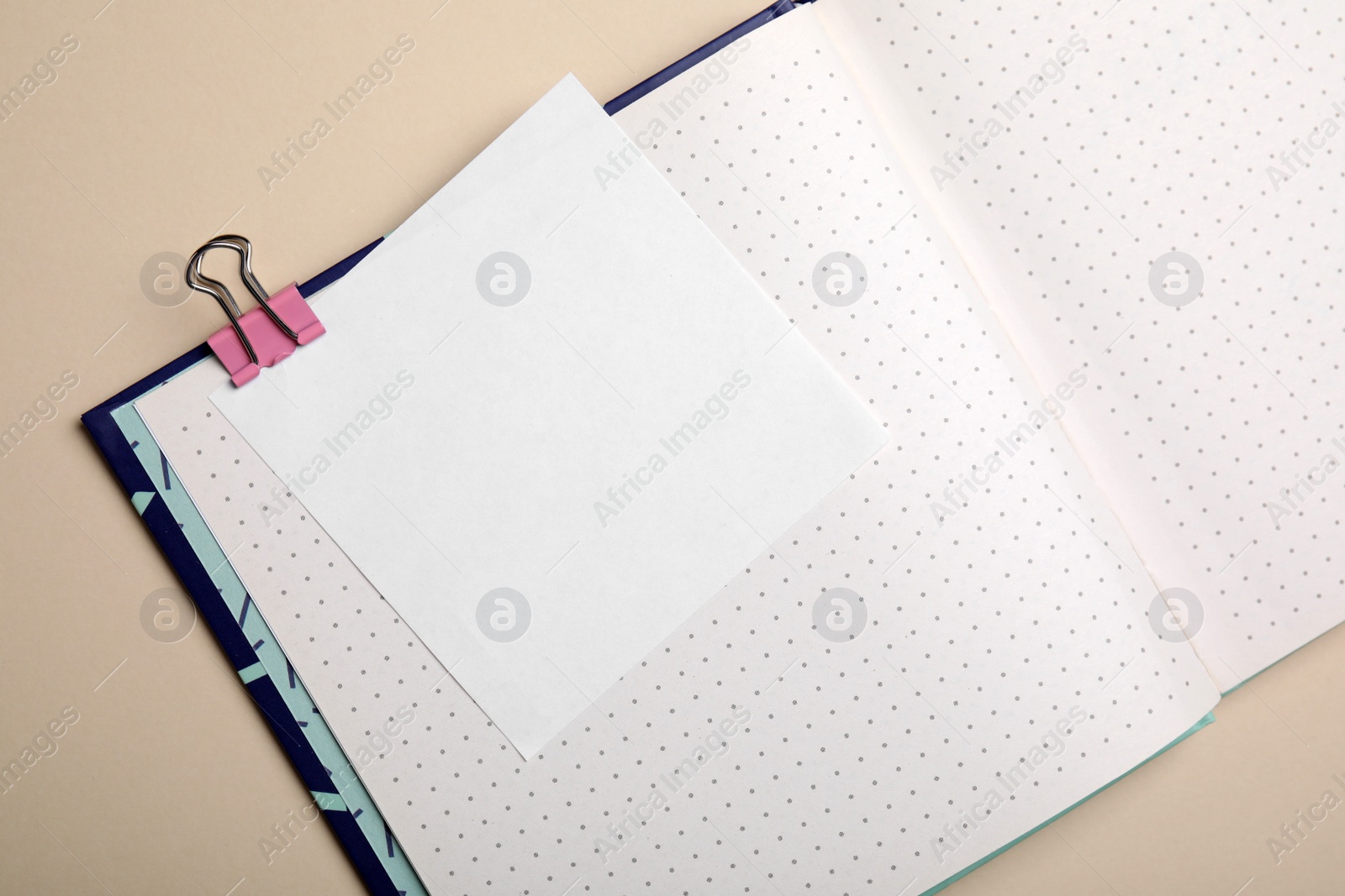 Photo of Notebook and note with paper clip on beige background, top view