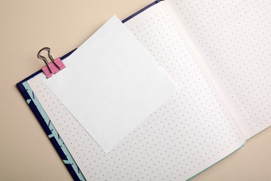 Photo of Notebook and note with paper clip on beige background, top view