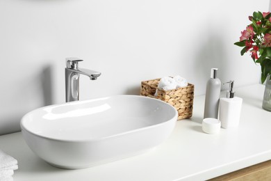 Photo of Vase with beautiful Alstroemeria flowers and toiletries near sink in bathroom