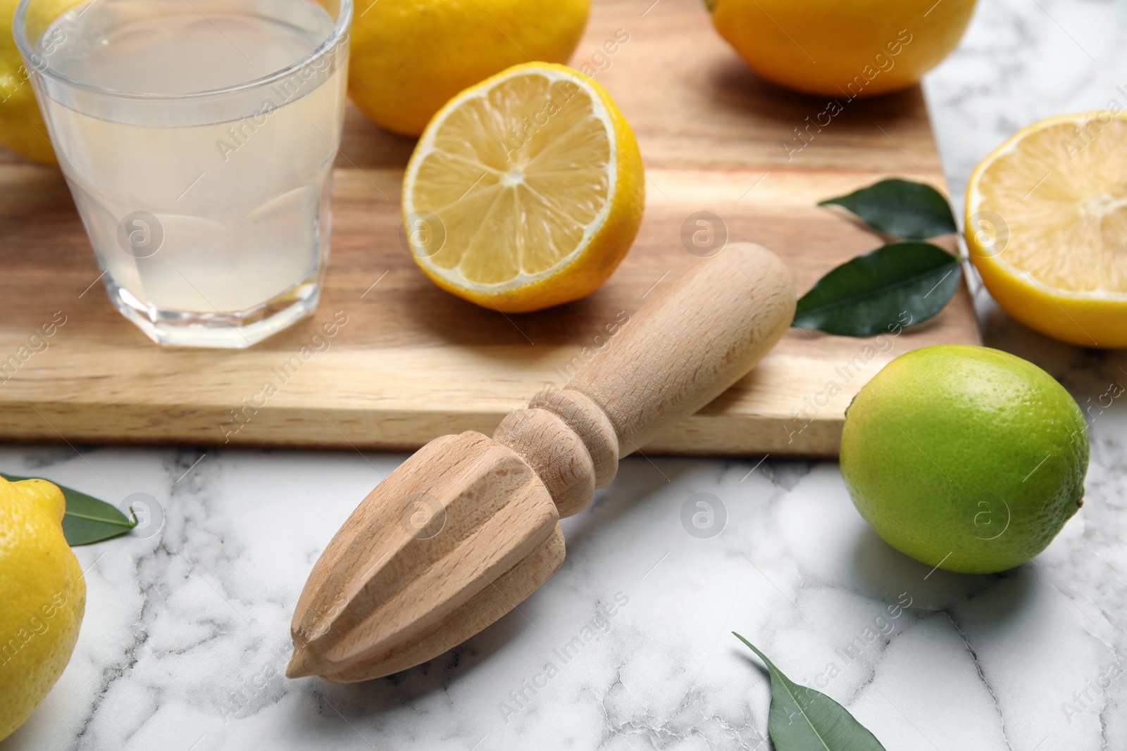 Photo of Wooden citrus reamer, fresh lemons and lime on white marble table