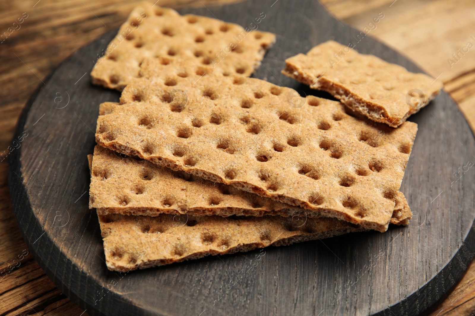 Photo of Board with fresh rye crispbreads on wooden table, closeup