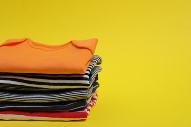 Stack of clean baby clothes on yellow background. Space for text