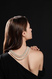 Photo of Young woman wearing elegant pearl necklace on black background, back view