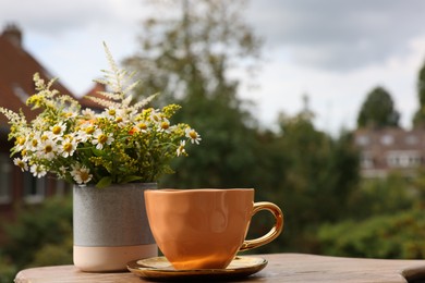 Photo of Cup of delicious chamomile tea and fresh flowers outdoors on sunny day. Space for text