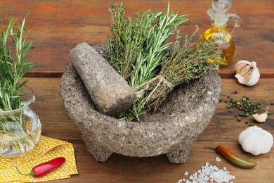 Photo of Mortar, different herbs, vegetables and oil on wooden table, closeup