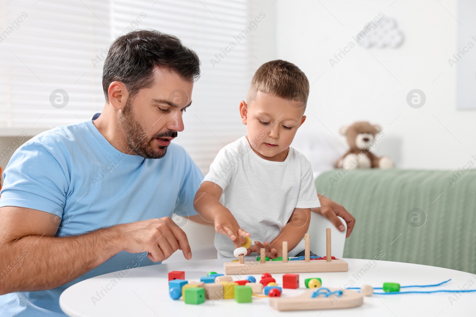 Photo of Motor skills development. Father and his son playing with stacking and counting game at table indoors