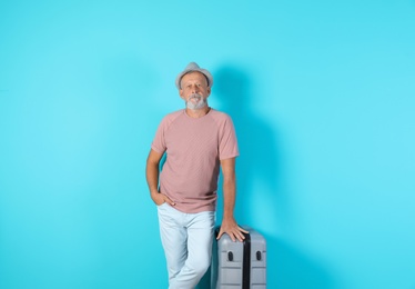 Senior man with suitcase on color background. Vacation travel