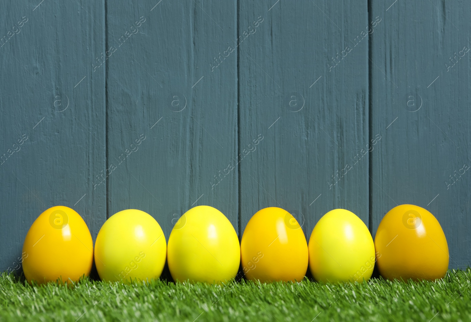 Photo of Bright Easter eggs on green grass against blue wooden background
