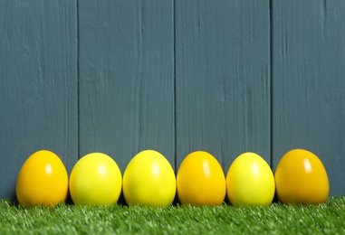 Photo of Bright Easter eggs on green grass against blue wooden background