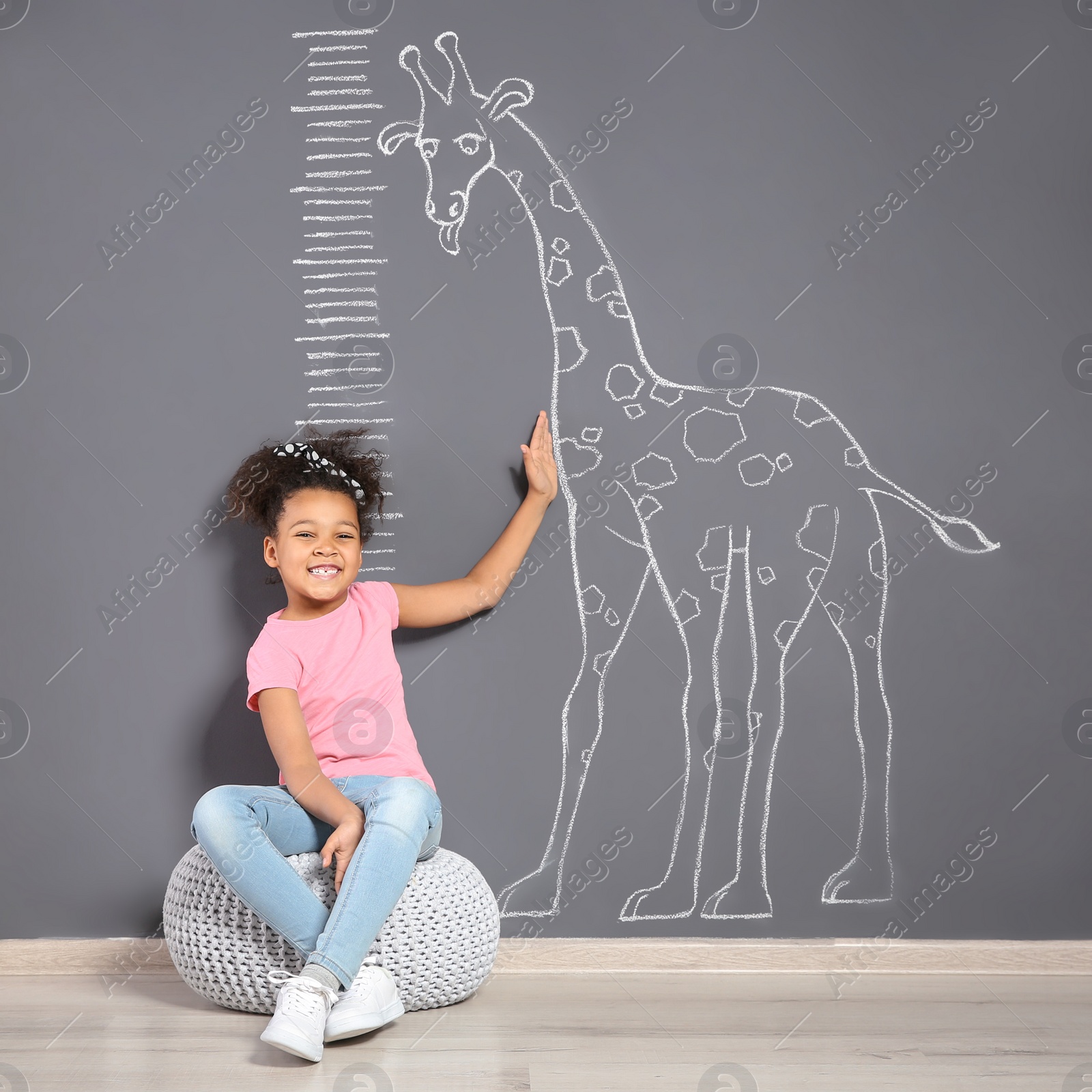 Photo of African-American child near grey wall with chalk giraffe drawing and height meter