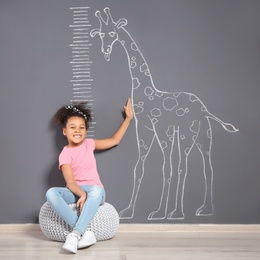 African-American child near grey wall with chalk giraffe drawing and height meter