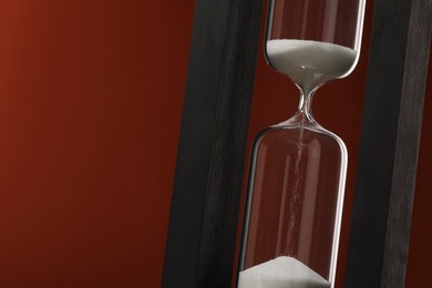 Photo of Hourglass with flowing sand on brown background, closeup. Space for text