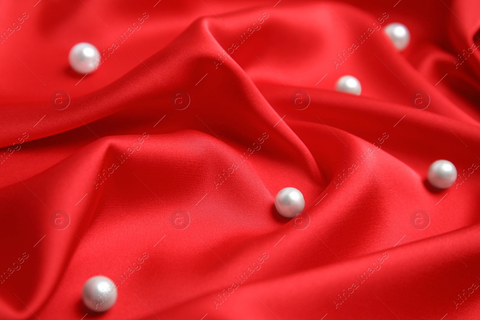 Photo of Many beautiful pearls on delicate red silk, closeup